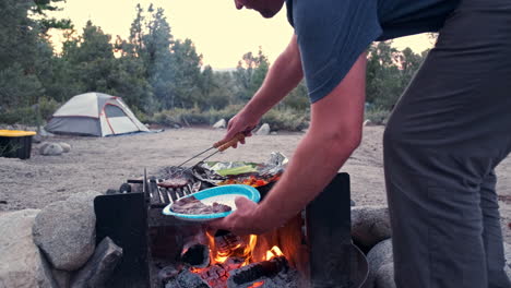 hombre cocinando en una fogata en el campamento, rodeado de pinos y carpas