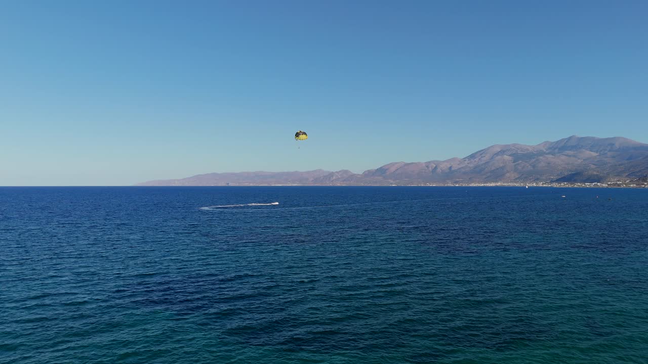 aérea - actividad de parasailing sobre el mar azul profundo con las montañas de creta en el fondo