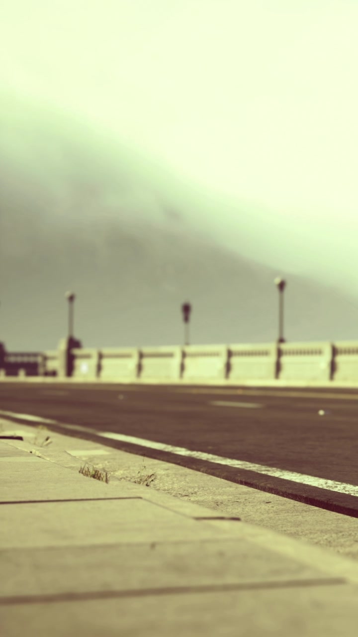 Cloudy view of a road alongside the sea with railings and lights