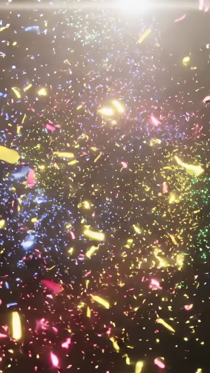 Video verticale: coriandoli luminosi che cadono su uno sfondo nero, retroilluminati da un bagliore dall'alto.