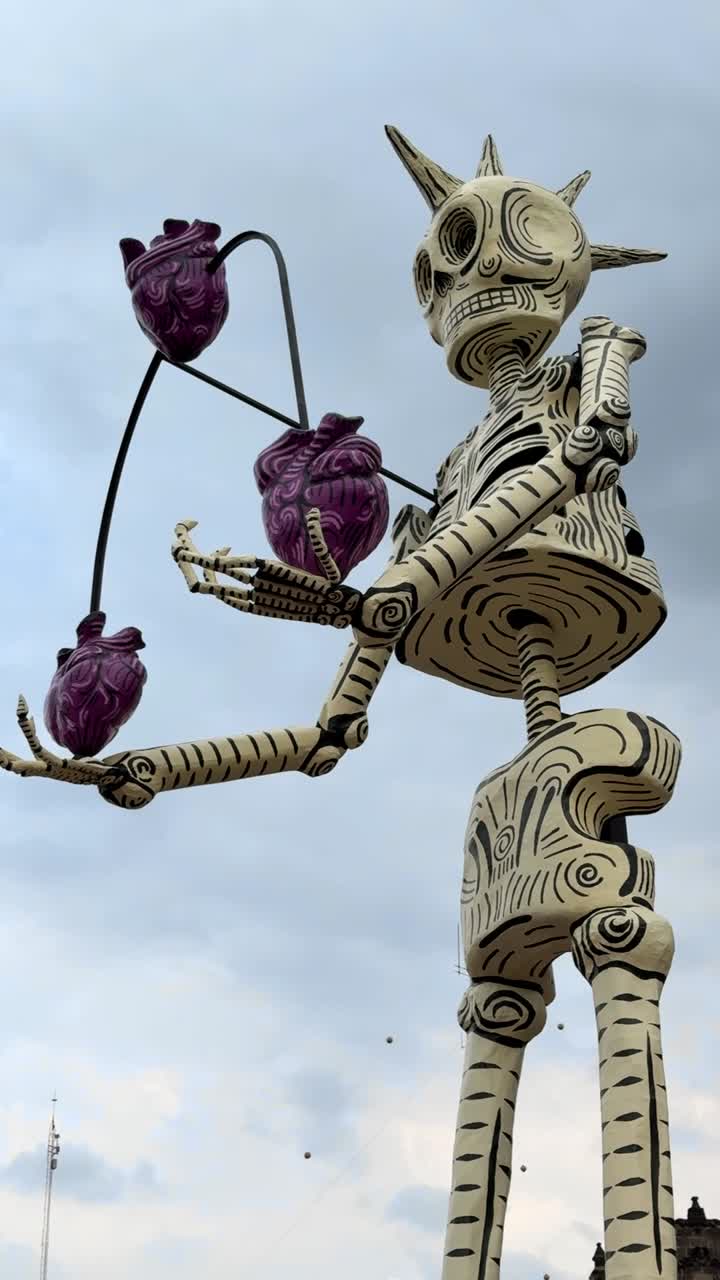 Giant skeleton sculpture with purple hearts celebrating Day of the Dead in Mexico against cloudy sky