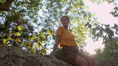 joven modelo de chica mirando a su alrededor sentada en la rama de un árbol