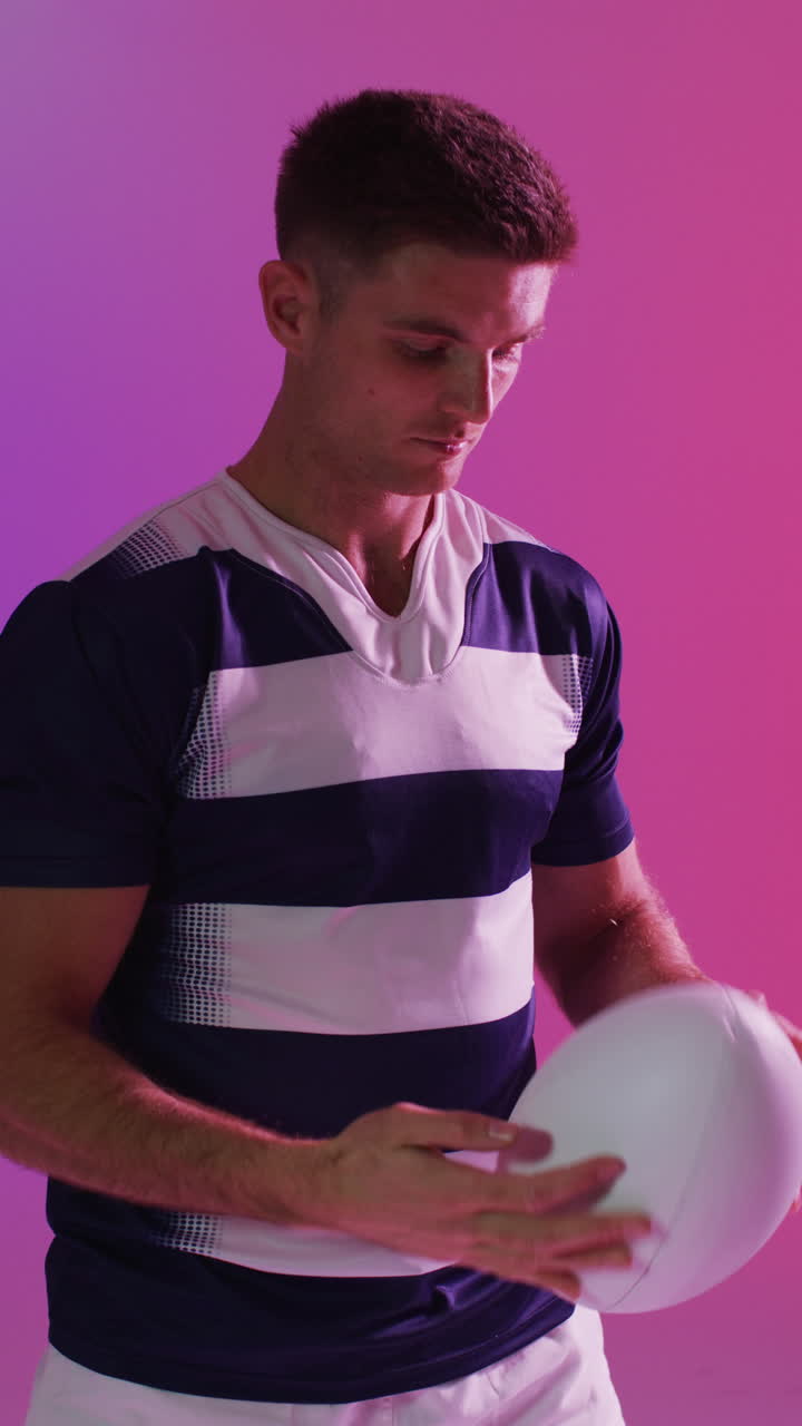 Video verticale di giocatore di rugby maschio caucasico con palla da rugby con illuminazione rosa.