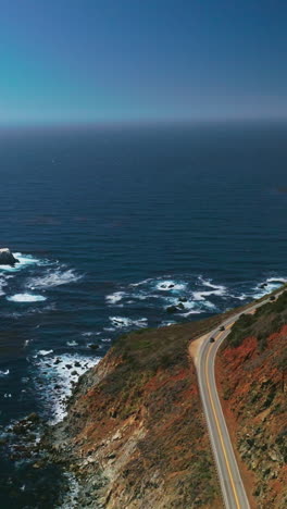 rocky shore with highway over cliffs. beautiful endless blue pacific ocean interflowing with clear azure sky. aerial view. vertical video