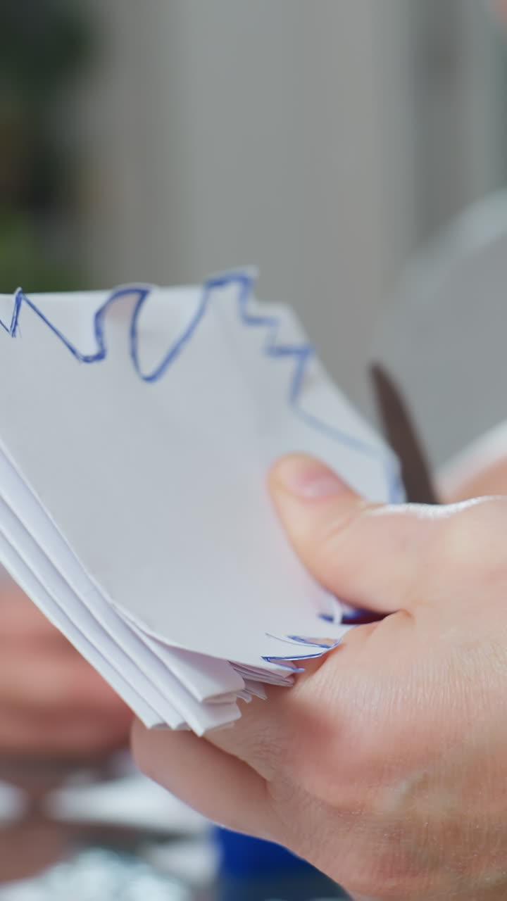 Primer plano de unas manos adultas blancas apilando hojas de papel, con un agarre firme y recortando láminas en capas, ambiente de clase o taller con una técnica de tijeras constante, demostración de estilo tutorial