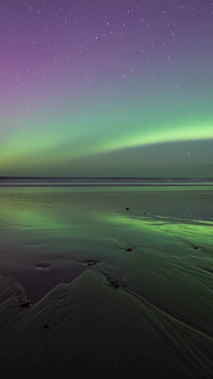 Video verticale: Fascia di aurora che si muove sopra una piana di marea, con vento solare in arrivo, riflettendosi sulla sabbia.