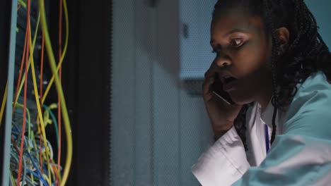 African-american-female-computer-technician-using-smartphone-working-in-business-server-room