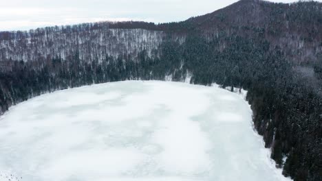 Lago-Del-Cráter-Volcánico-De-Santa-Ana-Cubierto-De-Hielo-Y-Rodeado-De-Bosques-De-Pinos-En-Invierno-En-Harghita,-Rumania