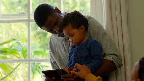 Front-view-of-black-father-and-son-using-digital-and-sitting-on-window-sill-of-comfortable-home-4k