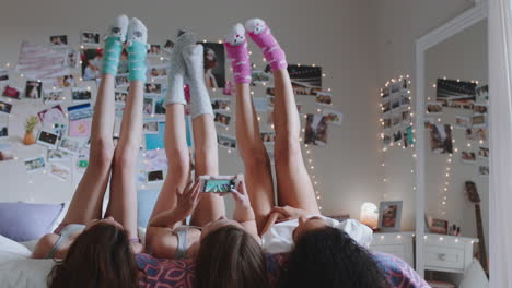 Chicas-Adolescentes-Felices-Acostadas-En-La-Cama-En-Casa-Con-Las-Piernas-Arriba-Divirtiéndose-En-Pijamas-Tomando-Fotos-Usando-Un-Teléfono-Inteligente-Disfrutando-De-Una-Relajante-Mañana-El-Fin-De-Semana