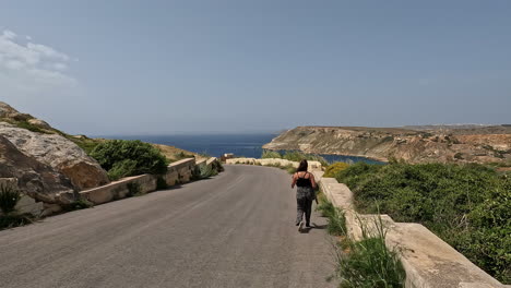 Frau-Geht-An-Einem-Sonnigen,-Windigen-Tag-Auf-Der-Straße-Mit-Blick-Auf-Das-Meer