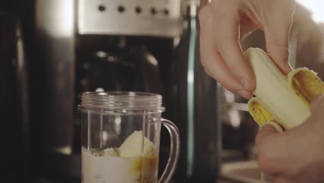 person making banana smoothie with milk in the blender for breakfast