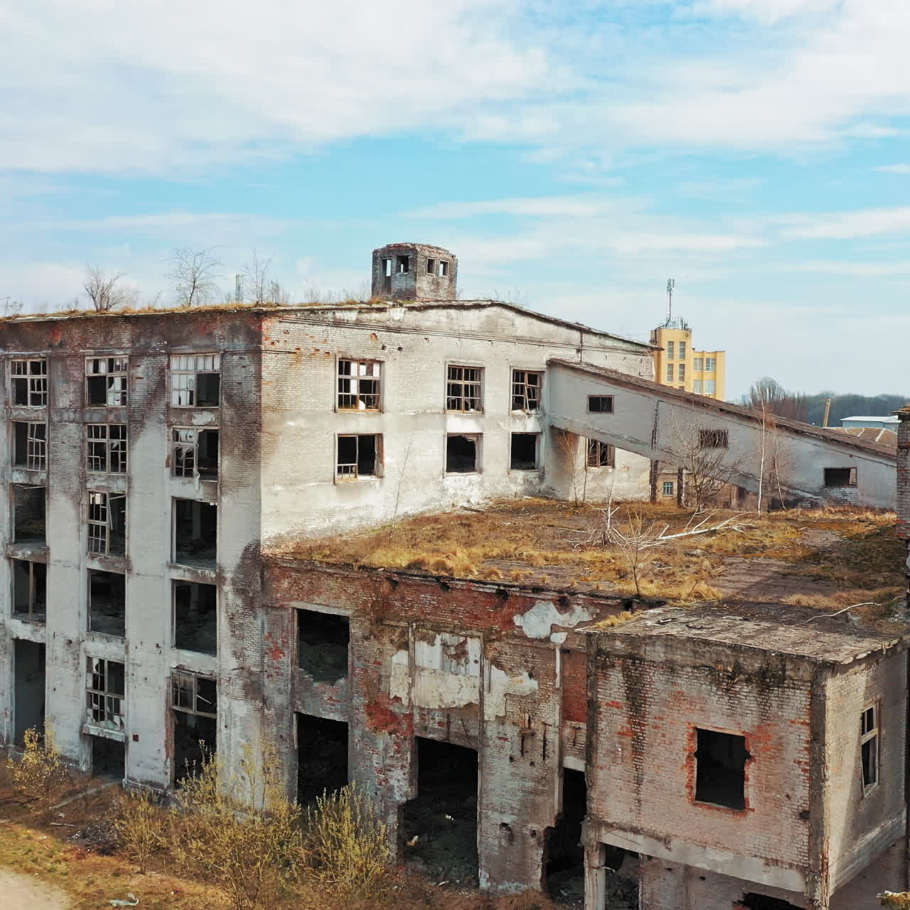 Aerial view of abandoned buildings, ruined after military actions. Destroyed industrial architecture with broken windows and big holes. Camera moves forward.