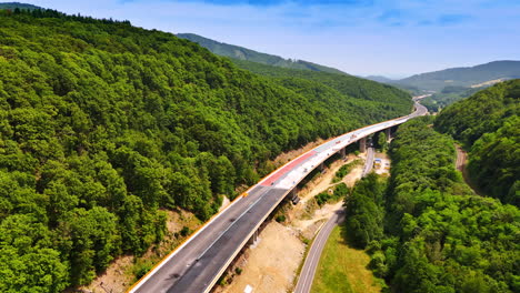 building of the freeway at the foot of green wooded mountains. cars go by the road under the new highway. aerial view