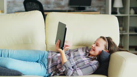 little girl lying on the couch using her tablet