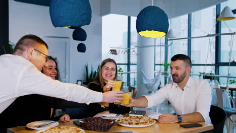 happy people sitting at the dinner table cheering and clinking glasses with juice. friendly smiling colleagues having pizza at café.