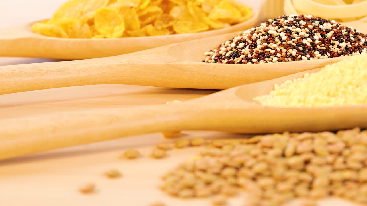 Close-up of quinoa, lentils, couscous, and cornflakes in wooden spoons. Warm lighting enhances texture and color contrast