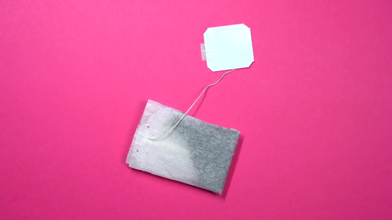 Tea bag with white label slowly spinning on a rotating pink background.