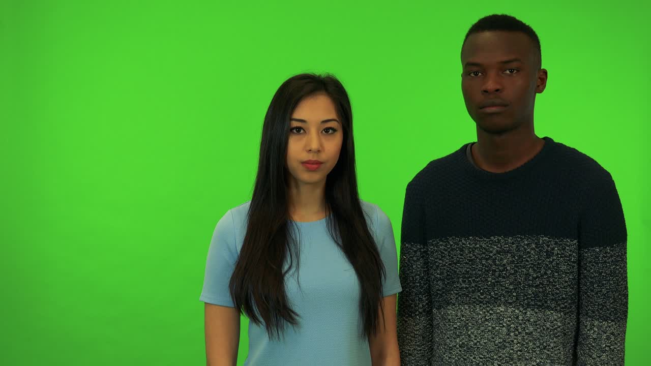 Uma jovem mulher asiática e um jovem homem negro balançam a cabeça para a câmera - estúdio com tela verde.