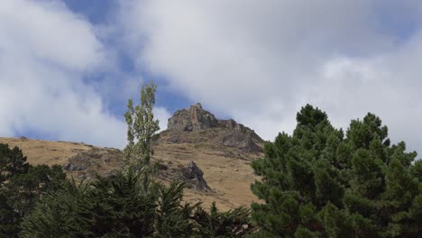 Volcanic-rock-on-hillside-contrasts-with-gentle-movement-of-clouds-and-trees---Castle-Rock,-Horotane-Valley