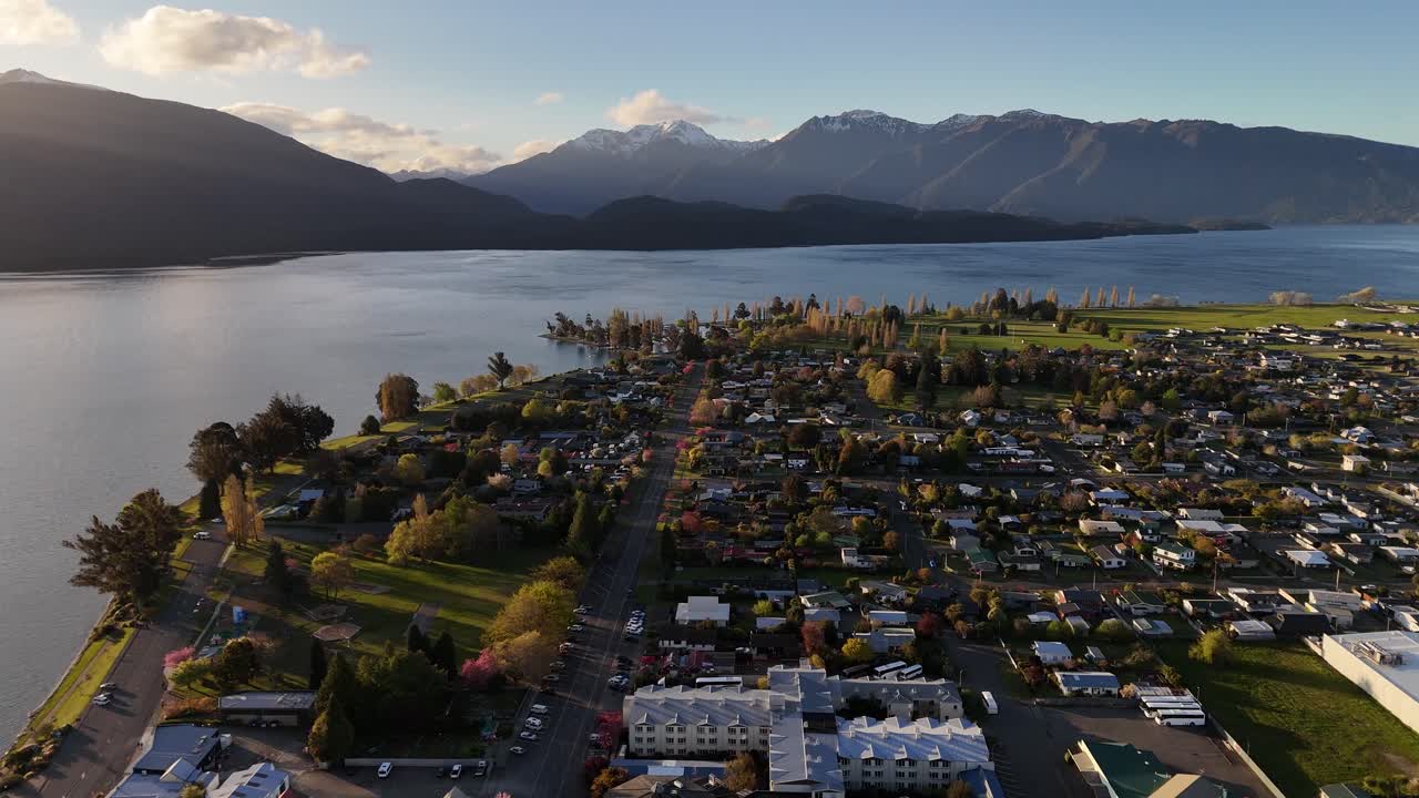 Scenic 4K aerial drone footage flying over Te Anau town towards the lake at sunset. Panoramic view of Fiordland region, streets, and majestic mountains on New Zealand's South Island