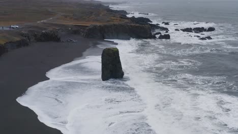 sea stack protruding on the coastline of black sand beach in stapavik in eastern iceland