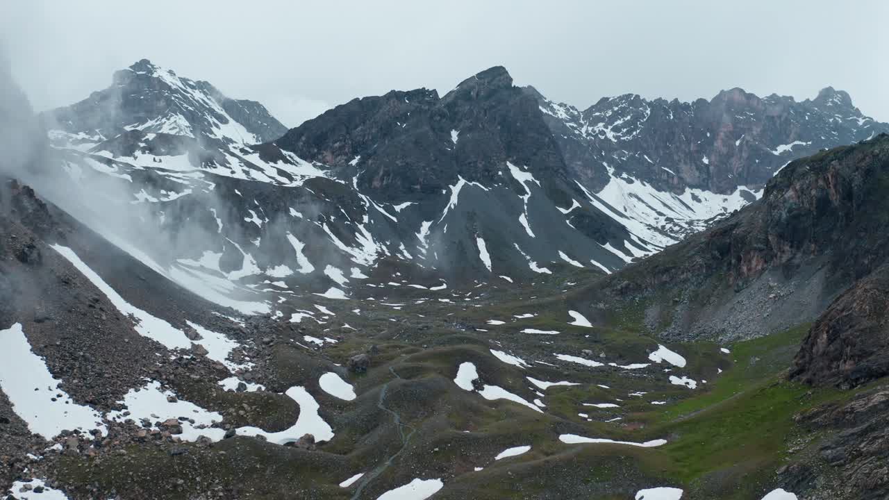 Kar yamaları ve görünen Cascata di Stroppia, Lago Niera ile sisli dağ manzarası.