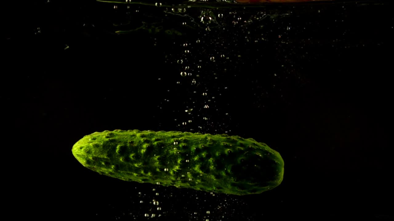 Caída de pepino en agua. Cámara lenta. Fondo negro.