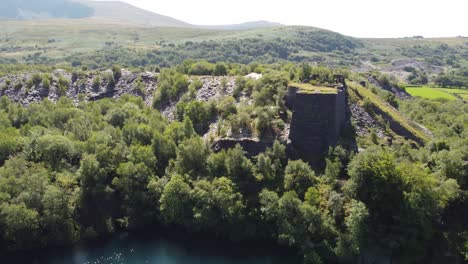 Vista-Aérea-Orbitando-El-Bosque-De-La-Cantera-De-Pizarra-Dorothea-Con-Las-Montañas-Snowdonia-Al-Fondo