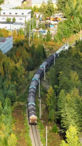 vertical drone shot following a long cargo train in middle of fall colored forest
