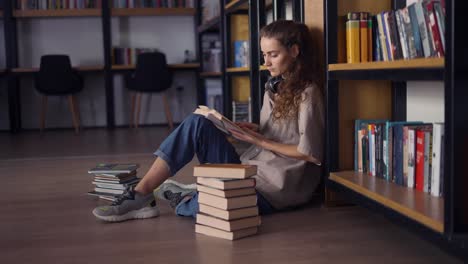 estudiante de sexo femenino pensativo sentado contra una estantería con libros en el suelo