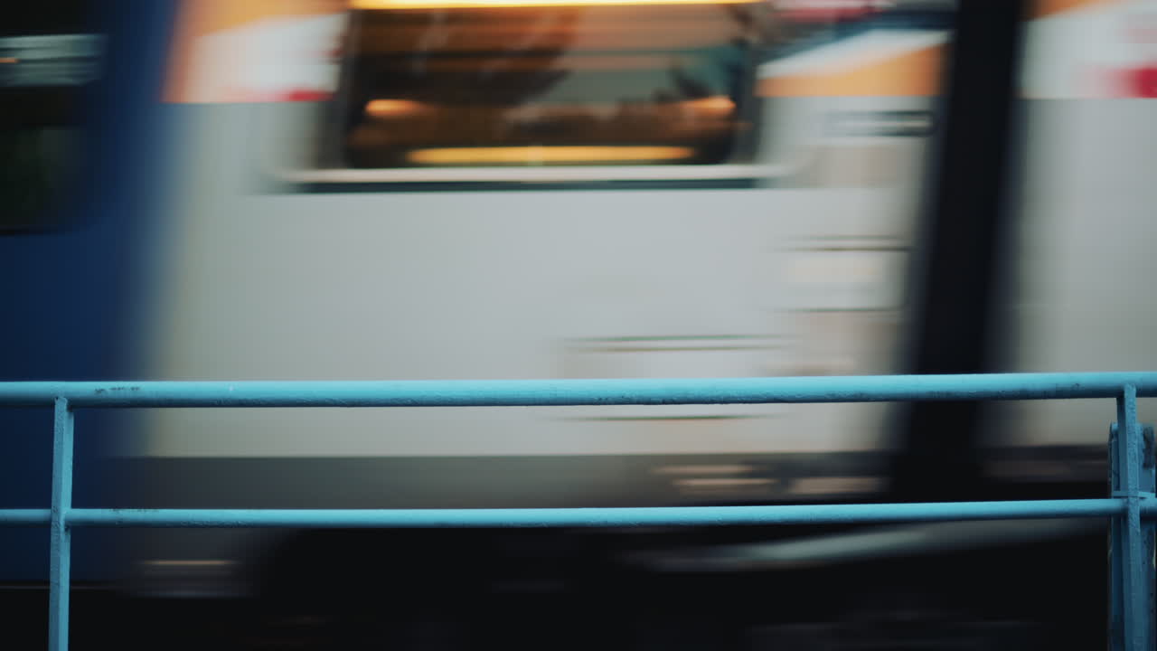 Blurred motion of a train passing behind a blue metal fence with soft background colors