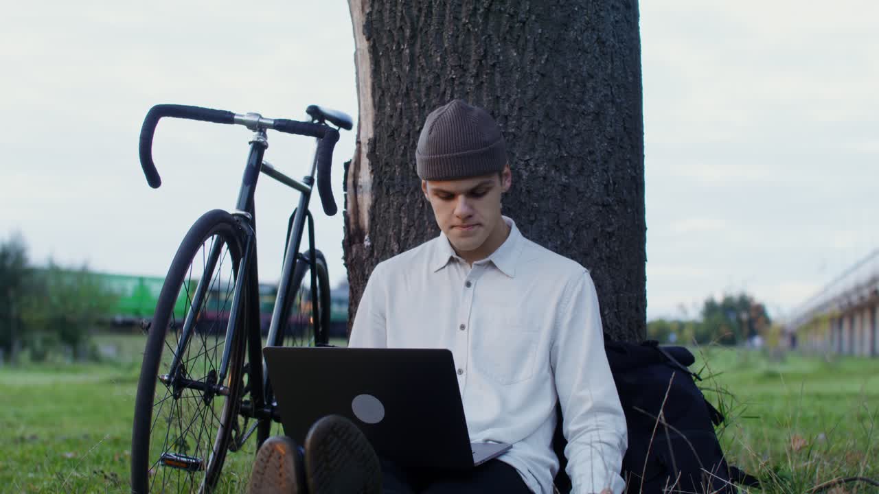 joven trabajando al aire libre con computadora portátil y bicicleta
