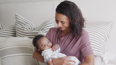 millennial african american mother sitting up in bed holding her baby, close up