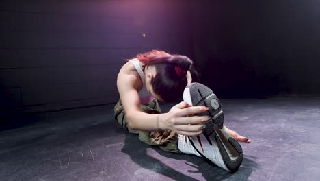 young female dancer with red hair performing front splits showing his flexibility skill in studio with black background, fitness woman modern dance concept