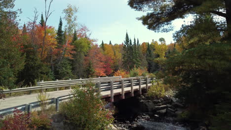 Aerial-ascending-over-Asphalt-road-viaduct-above-river,-surrounded-by-Autumnal-colorful-foliage