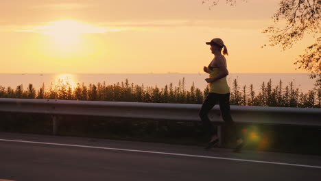 Aktive-Frau,-Die-Bei-Sonnenuntergang-Joggt,-Läuft-Entlang-Der-Straße-Entlang-Des-Meeres-Steadicam-Folgen-Schuss