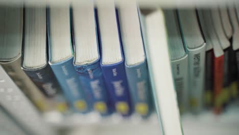 una mano mueve el dedo a lo largo de las espinas del libro hasta elegir uno de los libros