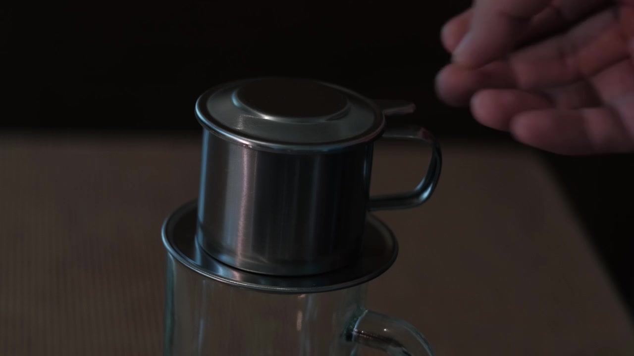 Nærbilde, statisk opptak av en hånd som plasserer lokk på et tradisjonelt vietnamesisk phin-filter under kaffebryggingsprosessen