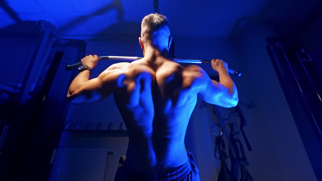 Brutal strong athletic men pumping up muscles. Doing workout on sport equipment - muscular bodybuilder doing exercises in gym with naked torso. Fitness and bodybuilding concept. Video from the back.