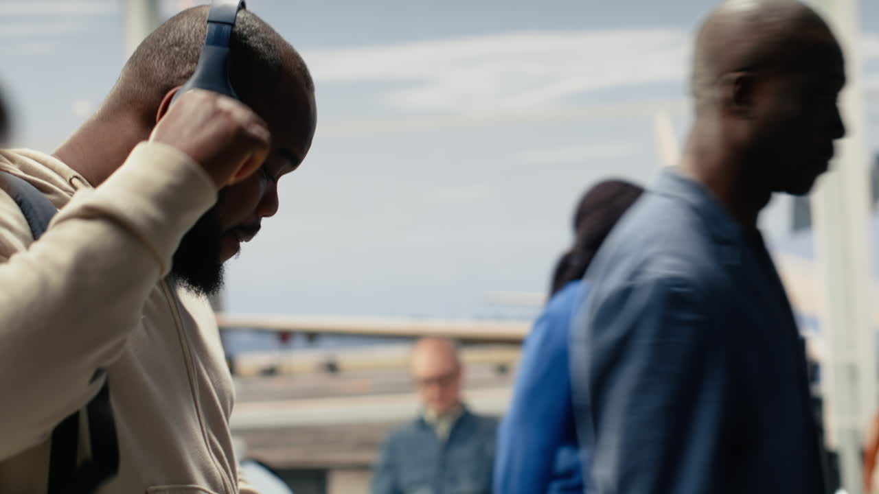 Uomo che si muove in un corridoio affollato dell'aeroporto con le cuffie audio indossate.