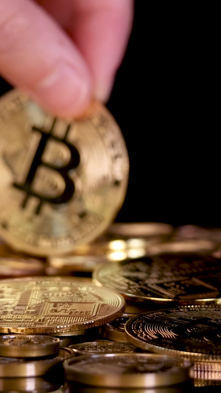Tomada macro vertical de uma mão soltando uma moeda de criptomoeda dourada e brilhante sobre tokens.