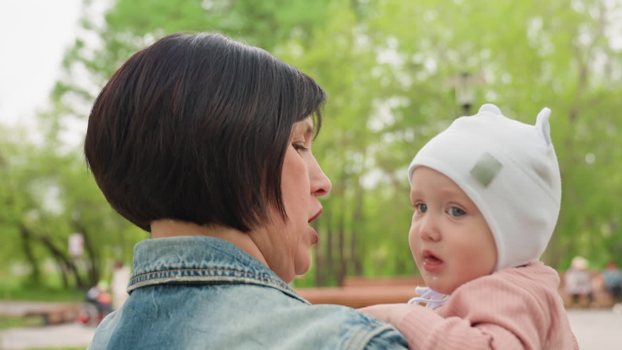 Mother And Infant Amidst Greenery And Benches, Woman Holding Baby Surrounded By Trees And Park Benches, Gentle Scene Of Mother And Infant Sharing Tender Moment Amongst Park Elements