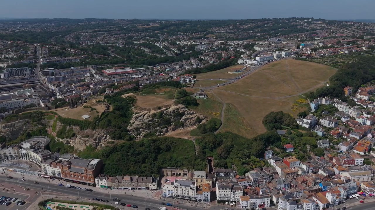 Panoramica aerea del Castello di Hastings e di West Hill che rivela il lungomare, i negozi del centro città, le strade, i parchi e i quartieri circostanti a Hastings, East Sussex, Inghilterra