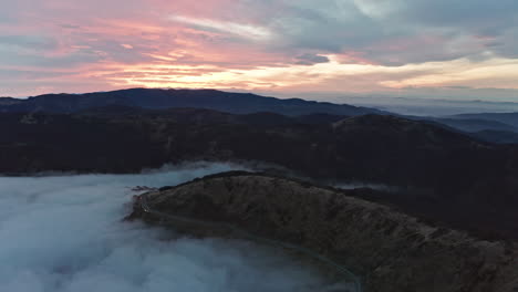 Misty-mountain-roads-at-sunrise-with-soft-clouds-and-gentle-light,-aerial-view