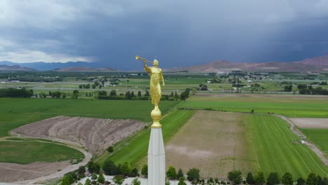Symbolic-Angel-Moroni-Statue-Sculpture-on-LDS-Mormon-Temple-in-Payson,-Utah---Aerial-Drone-Orbit-with-Lightning-Thunderstorm