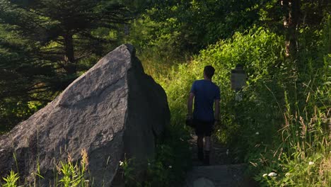 Hiker-on-a-trail-walks-by-a-huge-pointed-granite-rock-in-the-forest