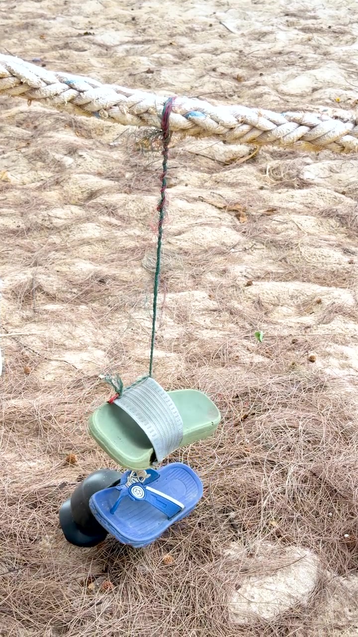 Discarded sandals and fishing gear hang from a thick rope over sandy beach ground
