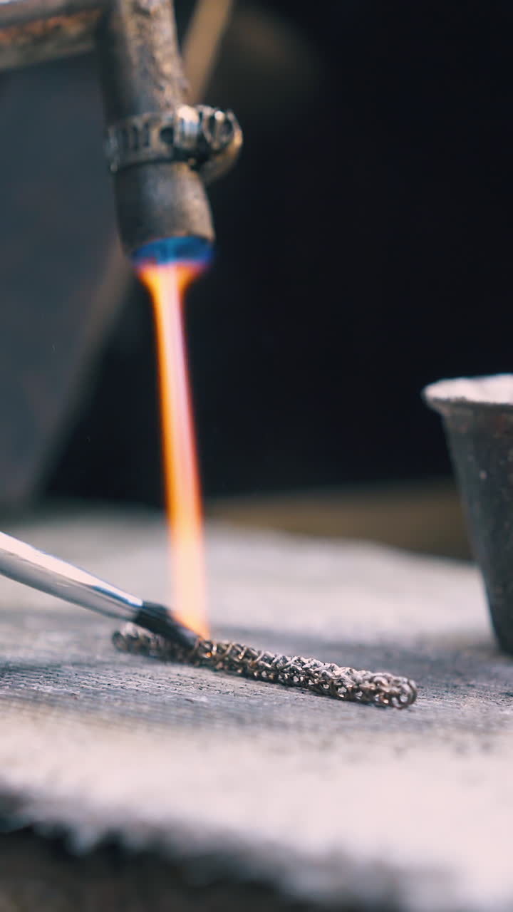 CU shot: skilled jeweler applies special material on heated decorative chain with brush on asbestos sheet closeup