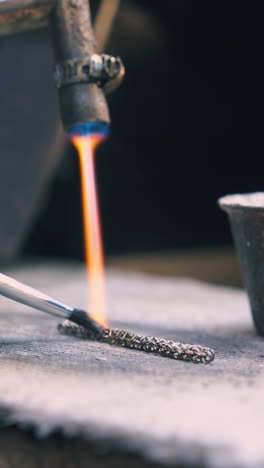 cu shot: skilled jeweler applies special material on heated decorative chain with brush on asbestos sheet closeup